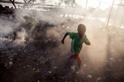 A boy runs through the smoke of burning garbage near the Niger River in Bamako, Mali on December 9th, 2012.